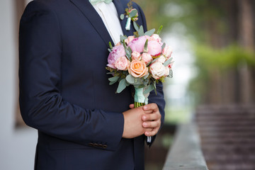 the groom waiting for the bride holds in hand a bouquet from pink peonies. Wedding day