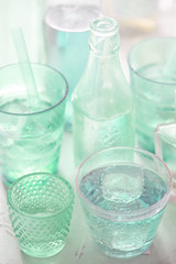 Various green bottles and glasses with drinks and ice cubes 