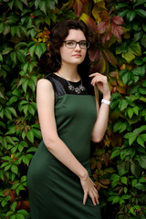 Slender brunette girl in green dress with spectacles in ivy