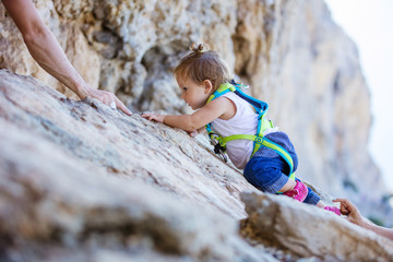 Little girl climbing up cliff, father and mother safeguarding her