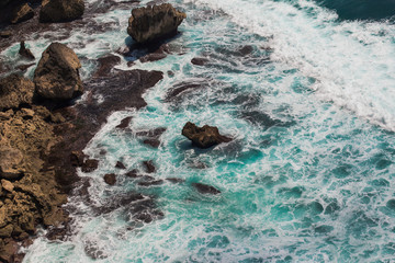 Indian ocean waves and rocks. Turquoise sea water with white foam meet rough stone rocks on the shore. Powerful and peaceful nature concept.