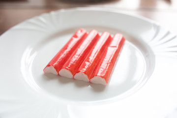 Four red crab sticks on a white plate - imitation, surimi.