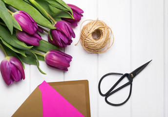 Tulips, scissors and envelope with pink paper on the white table
