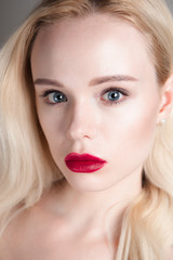 Fototapeta na wymiar Beauty model girl with perfect make-up red lips and blue eyes looking at camera. Portrait of attractive young woman with blond hair. Beautiful female face with clear fresh skin. Fashion close up shot.