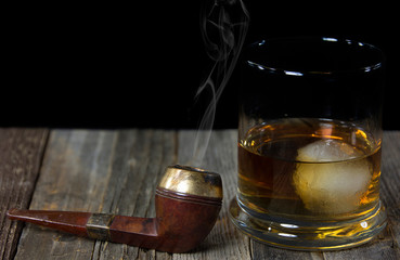 vintage smoking pipe on weathered wood with whiskey drink