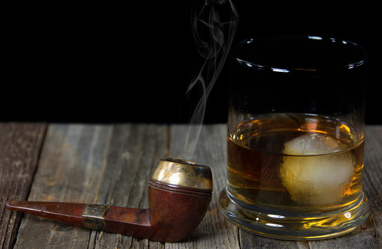 vintage smoking pipe on weathered wood with whiskey drink