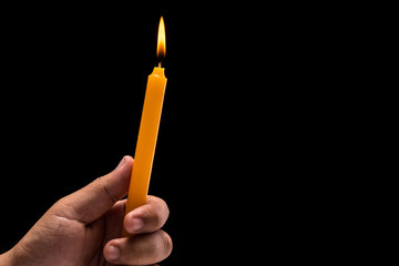 Hand holding light burning candle. Studio shot isolated on black background