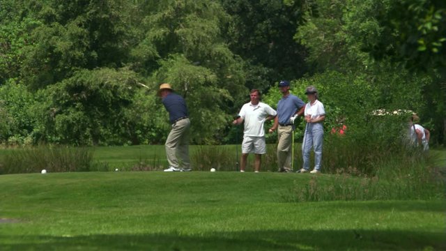 Men and women golfers watching as one player and then a second hit balls 