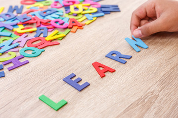 Colorful wooden alphabet and word "LEARN", Hand sort on N. Top view on grey wooden table