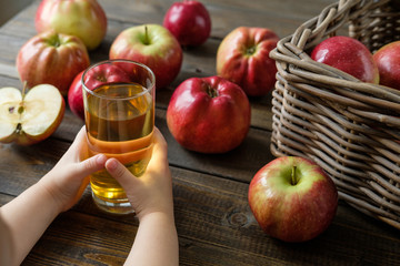 a glass of juice in children's hands on a background of red ripe apples