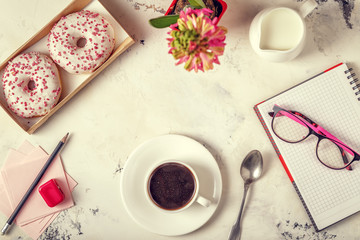 Notepad, donuts and coffee on white table.