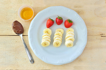 Fruits - banana and strawberry - with honey and hazelnut cream on a wood table