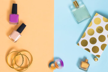 Beauty products and accessories still life on colorful background. Nail polishes, golden bracelets, notepad, perfume.