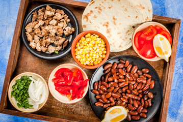 Ingredients for Mexican food on a tray: beans, stew beef, corn, tomatoes, red pepper, onion, herbs, tortillas taco, top view copy space