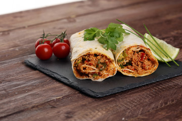 Delicious homemade vegetarian couscous wrap with tomatoes, carrots, zucchini, yellow bell pepper and fresh basil on a dark rustic wooden kitchen table