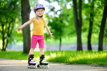 Pretty little girl learning to roller skate on beautiful summer day in a park