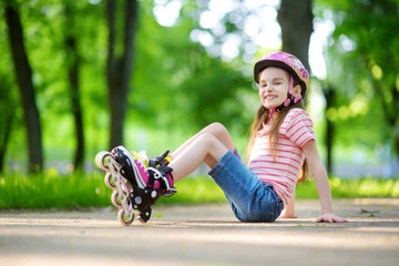 Pretty little girl learning to roller skate on beautiful summer day in a park