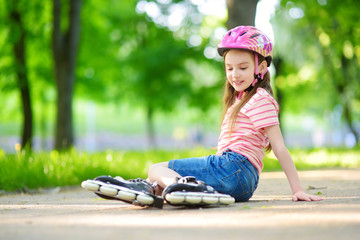 Pretty little girl learning to roller skate on beautiful summer day in a park