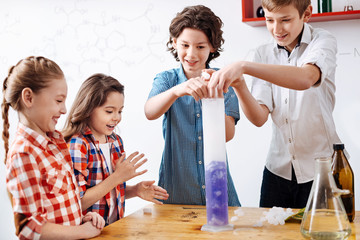Positive delighted boys putting some chemical reagents to a retort