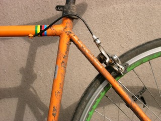 Rostiges altes Rennrad und Herrenrad in Orange mit Felgenbremse bei Sonnenschein im Hafenviertel...