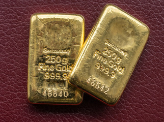 Two cast gold bars weighing 250 grams on the background texture burgundy leatherette.