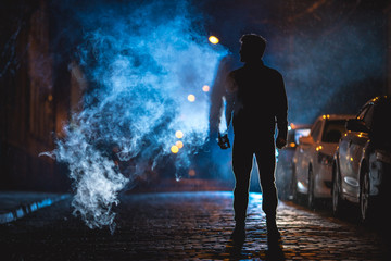 The man smoke on the street. Evening night time. Telephoto lens shot