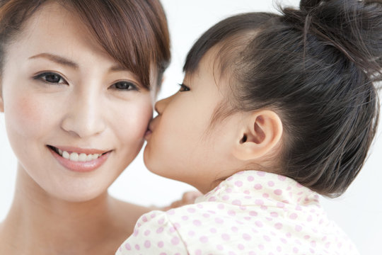Girl kissing mother, woman looking at camera, close up, white background
