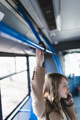 Fototapeta na wymiar Beautiful young woman standing in city bus and talking on mobile phone. Selective focus on woman's hand.