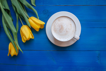 Coffee mug with yellow tulip flowers and notes good morning on blue rustic table from above, breakfast on Mothers day or Womens day .Spring  flowers bouquet