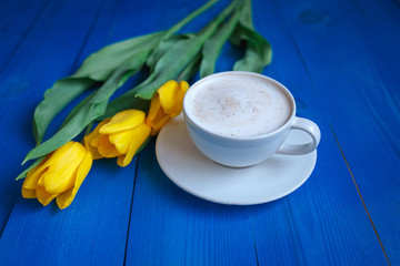 Coffee mug with yellow tulip flowers and notes good morning on blue rustic table from above, breakfast on Mothers day or Womens day .Spring  flowers bouquet