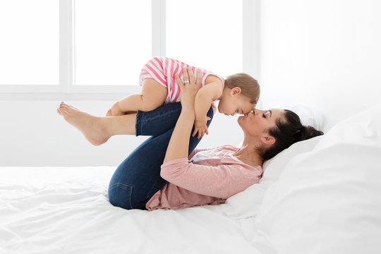 Mom lying on a bed holding her baby up on her knees and kissing her forehead