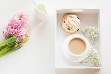 Morning breakfast in spring with a cup of black coffee with milk and pastries in the pastel colors, a bouquet of fresh pink hyacinth on a white background. Top view.