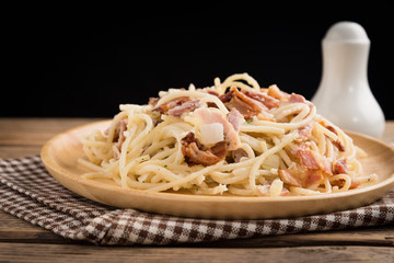 delicious meat italian pasta spaghetti with ham peas and white sauce on wood table.
