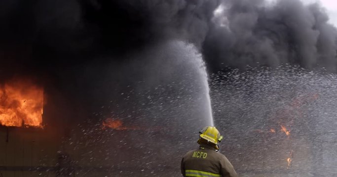 A fully engulfed structure fire belches black smoke as firefighters shoot streams of water from three directions