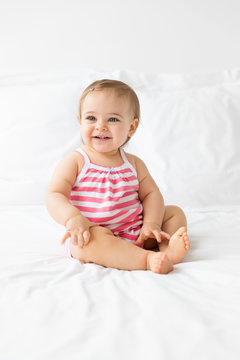 smiling baby sitting on a white bed looking away