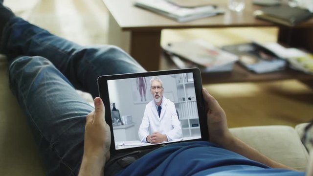 Sick Man Lying on a Couch and Having Video Conversation with His Doctor on a Tablet Computer. Shot on RED Epic Cinema Camera in 4K (UHD).