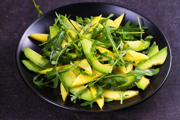 Avocado, mango and arugula salad on black plate