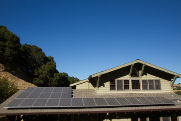 solar panels on roof of house. horizontal orientation, blue sky, gray panels on brown roof.