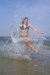 Young woman splashing in the shallow water of the sea, blurred motion