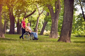 happy family time- senior man in wheelchair and daughter in the park.