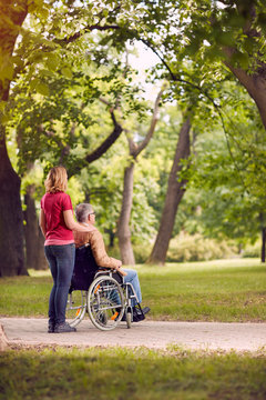 enjoying senior man in wheelchair and daughter in the park .