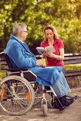 woman reading book outdoor her disabled father in wheelchair.