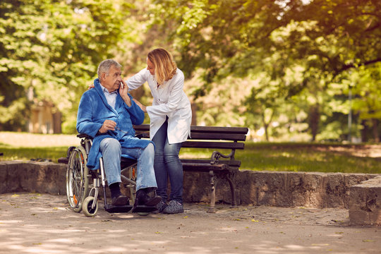Nurse helping elderly man on wheelchair.