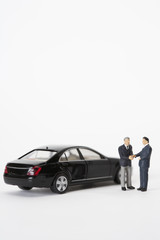 Two businessmen figurines shaking hands in front of a car