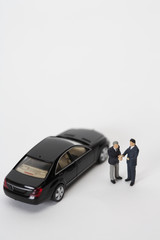 Two businessmen figurines shaking hands in front of a car