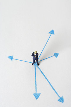 Businessman figurine standing in the middle of several arrows
