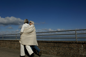 Two mature women wrapped in a blanket walking along the Baltic Sea