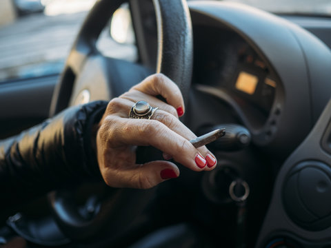 Cigarette in the hand with steering wheel of car