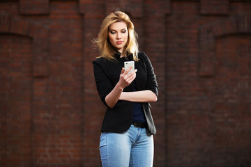 Fototapeta premium Young fashion blond business woman using smart phone on city street