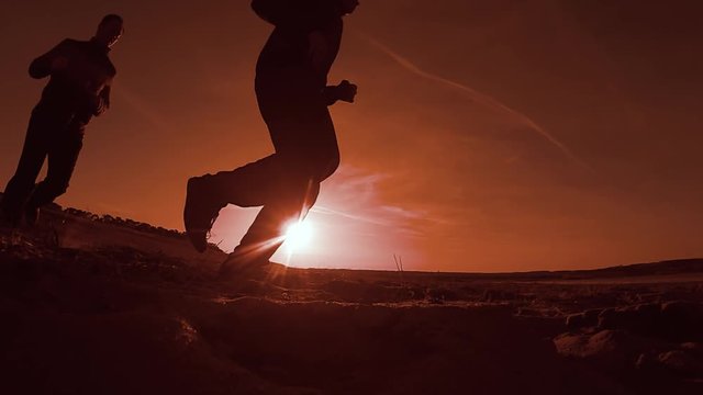 Two men running along the beach on the sand evening sunset sun, the runner